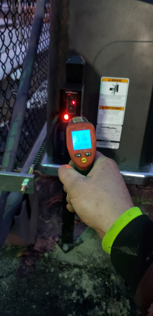 A thermal thermometer taking the reading of an automated gate's heated photo eye. The temperature is 51.6 degrees Fahrenheit