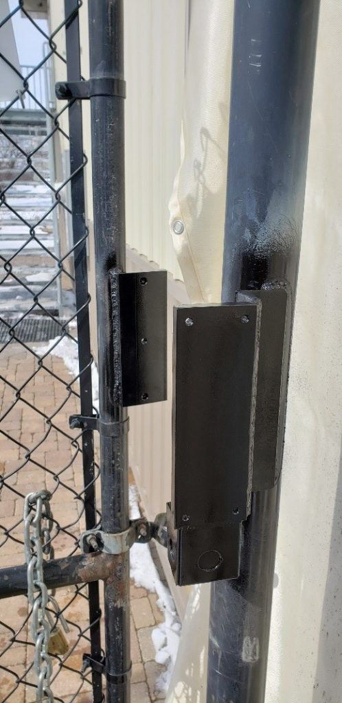 A chain link swing gate with a maglock welded to the gate frame and gate post