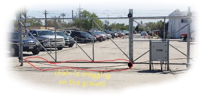 A chain link cantilever gate that has the chain from the slide driver dragging on the ground